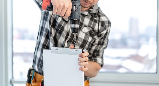 Man working using electric drill during process of wooden furniture manufacturing in workshop