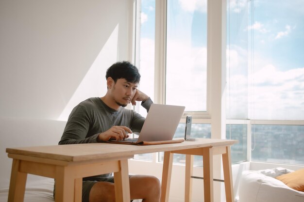 Photo man working with computer in apartment with city view at the windows in morning light