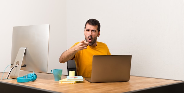 Uomo che lavora con laptot in un ufficio frustrato da una brutta situazione e che punta verso la parte anteriore