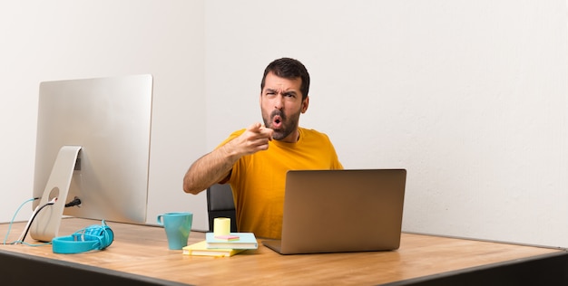 Man working with laptot in a office frustrated by a bad situation and pointing to the front