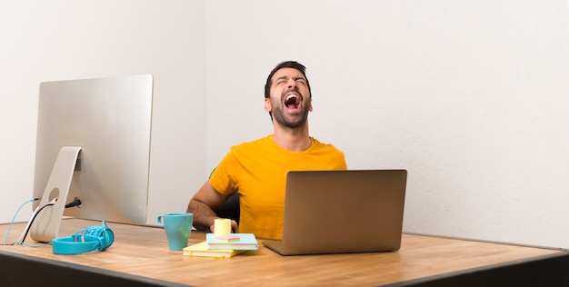 Man working with laptot in a office shouting to the front with mouth wide open