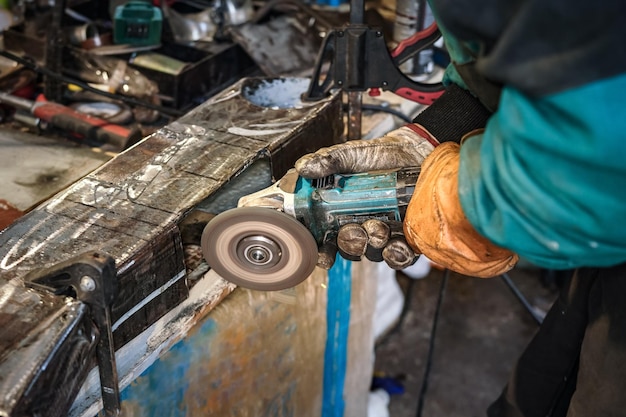 Photo man working with rotary angle grinder at workshop closeup detail to hands holding the tool