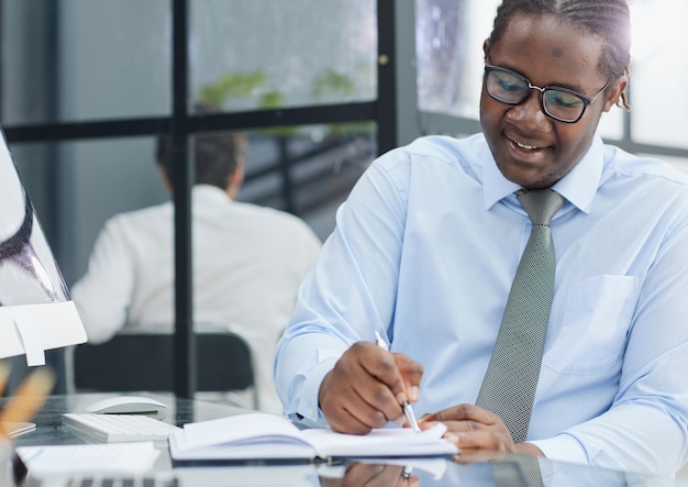 a man at a workplace at a table in front of a computer writes down notes