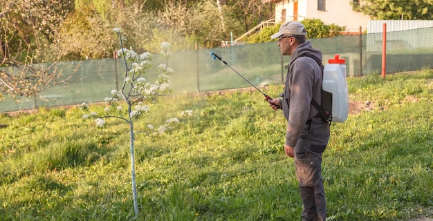 男は庭で働き、果樹の害虫に対して充電式噴霧器の化学物質を噴霧します