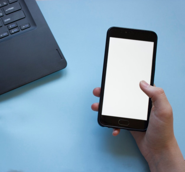 Man works at a laptop and holds a phone in his hand flatly.the problem of concentration at work while working from home.man distracted by phone while working from home on laptop.