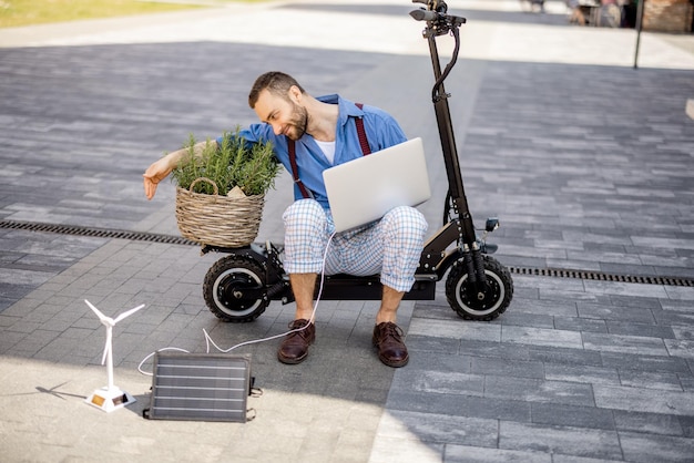 男は屋外の電動スクーターに座ってラップトップで動作します