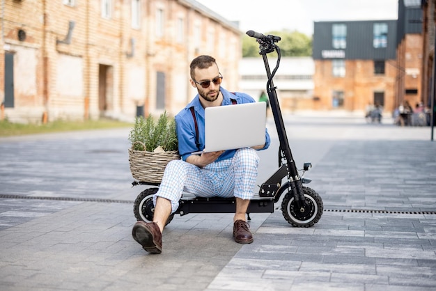 Man works on laptop while sitting on electric scooter outdoors