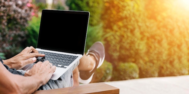 Un uomo lavora in natura seduto su una sedia con un laptop