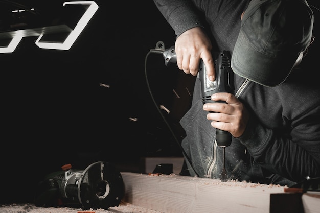 A man works with a drill in his workshop Carpenter drills with a hand power tool in a dark room with directional light