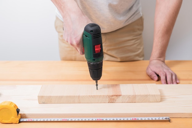 男は木製のテーブルで電動ドライバーを使って作業し、巻尺で測定も行います