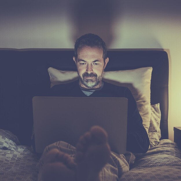 Photo man works with laptop lying on bed male home working remote office sitting in bedroom use devices