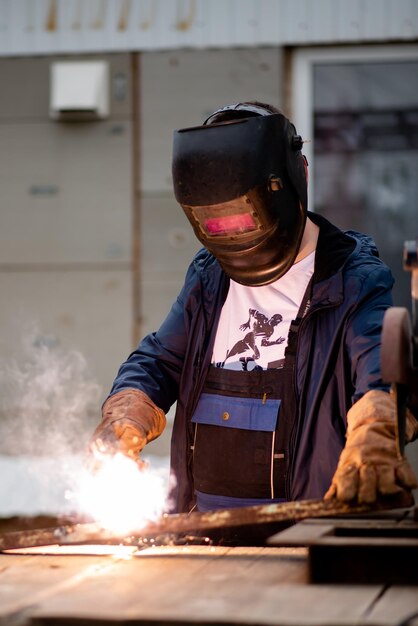 The man works with a welding machine He is wearing a welder's protective mask and protective gloves