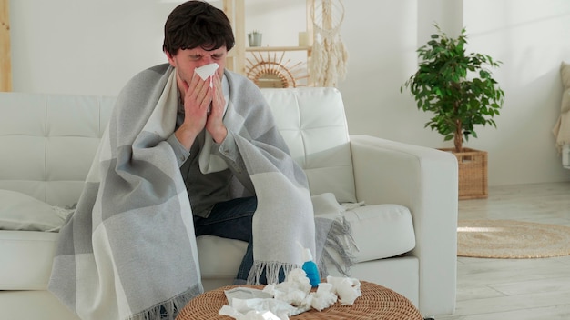 Man wrapped in a blanket feels sick with a cold and fever at home sick with the flu sitting on the couch