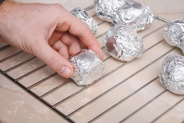 The man wraps peeled raw potatoes in foil and places them on the wire rack to bake them in the oven