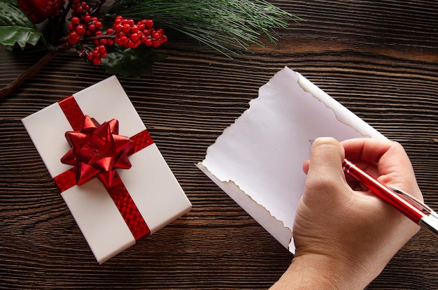 A man writes a postcard for the new year Nearby lies a gift with a red ribbon and a Christmas tree branch