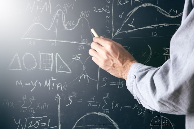 A man writes with chalk on a blackboard