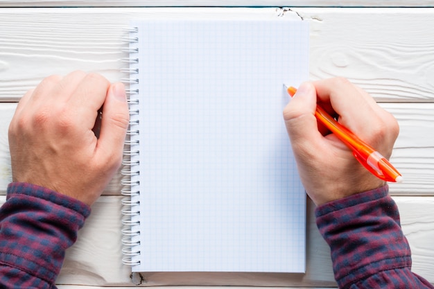 Man writing in a notebook on a white wooden background