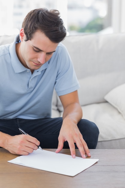 Man writing on a paper while he is sat on a couch