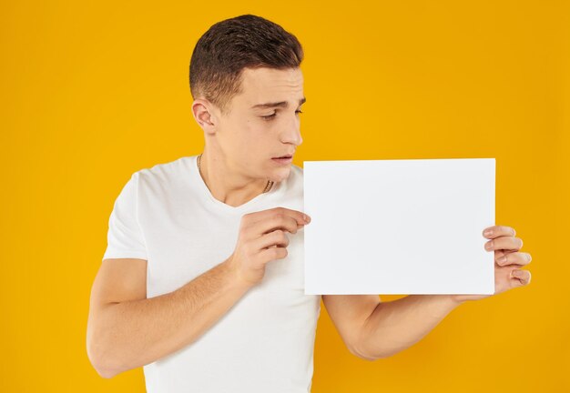 A man on a yellow background with a mockup in his hand a white sheet of paper person