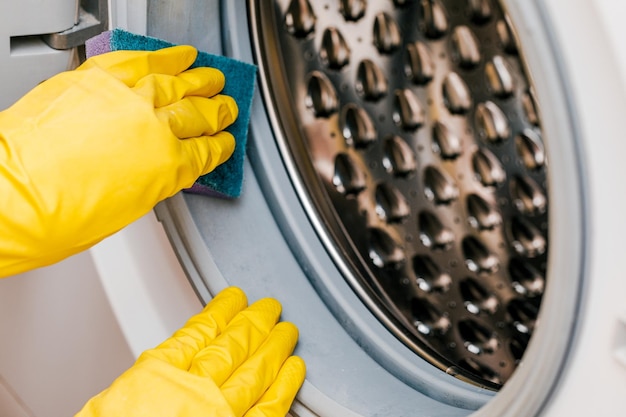 A man in yellow gloves cleans a dirty moldy rubber seal on a\
washing machine mold dirt limescale in the washing machine periodic\
maintenance of household appliances