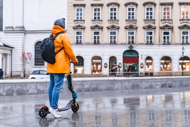 Man in yellow raincoat riding by city street at electric scooter