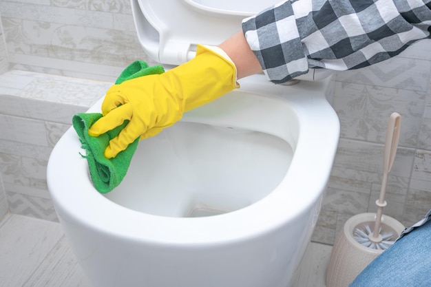 Man in yellow rubber gloves cleaning toilet seat with green cloth Bathroom and toilet hygiene Hand cleaning toilet bowl in bathroom