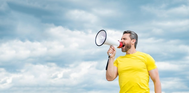 Man in yellow shirt shout in megaphone on sky background copy space