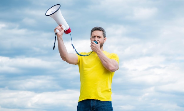 Man in yellow shirt shouting in loudspeaker on sky background