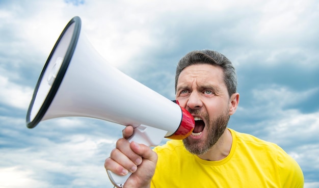 Man in yellow shirt speak in loudspeaker on sky background