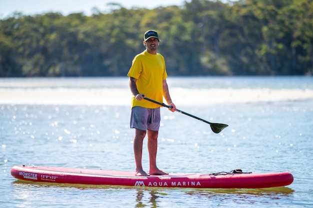 A man in a yellow shirt stands on a paddle board in the water with the words aqua marina on it.