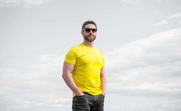 Man in yellow shirt and summer sunglasses outdoor on sky background