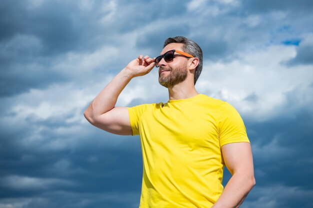 Man in yellow shirt and sunglasses outdoor on sky background copy space