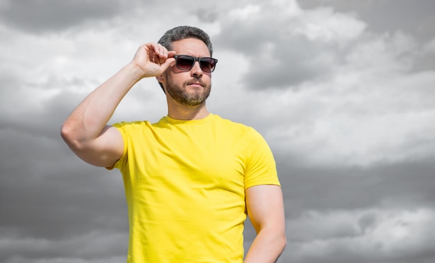 Man in yellow shirt and sunglasses outdoor on sky background with copy space