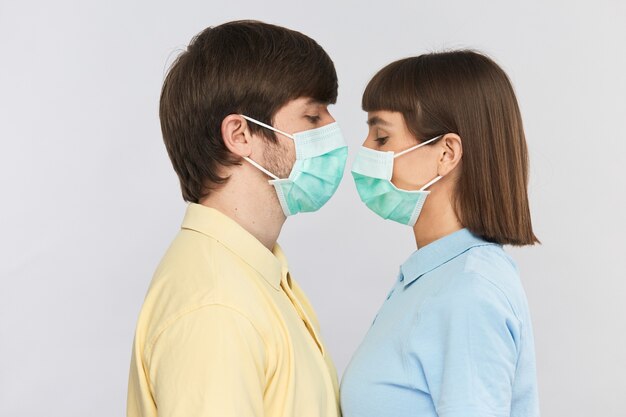 Man in yellow shirt and woman in blue shirt wear sterile mask and looking down standing face to face, protection mask on people while covid-19