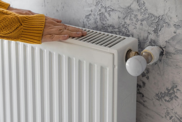 Man in yellow sweater warming his hands on the heater at home during cold winter days