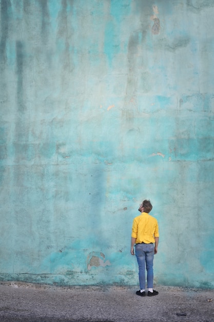 Uomo in maglietta gialla alzando lo sguardo su un muro