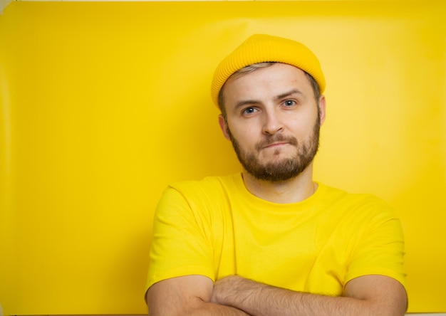 A man in a yellow T-shirt, standing on an isolated yellow background, crossed his arms and looks seriously at the camera