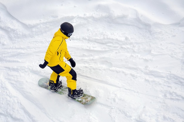 Man in yellow tracksuit helmet with glasses snowboarding downhill