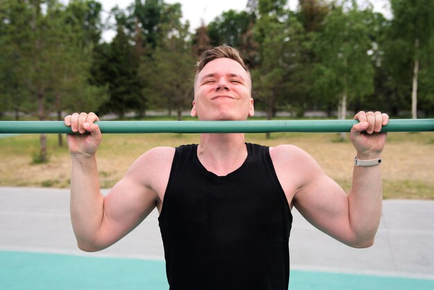 man young fitness strong athletic guy pulls himself up on the horizontal bar outdoors at gym