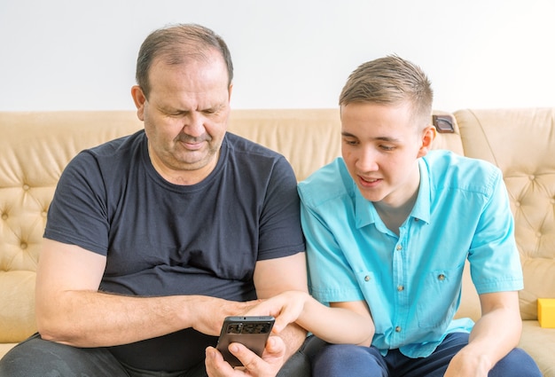 A man and a young man sit on a sofa and look at the phone screen