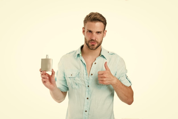 Man zelfverzekerd gezicht beveelt parfum aan toont duim omhoog gebaar Man met borstelfles parfum hij houdt van deze geur Mannelijk geurconcept Man knap beveelt aangenaam aroma aan voor man