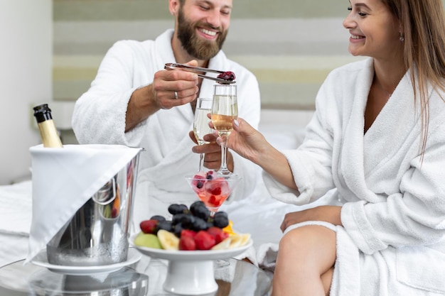 Man zet bessen in een glas mousserende wijn aan zijn vrouw in een hotel in bed