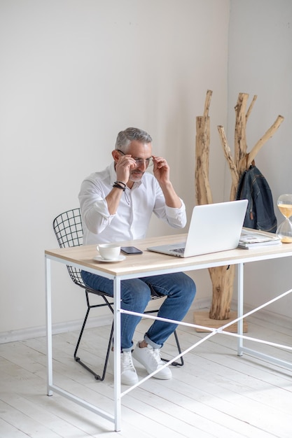 Man zet een bril op die aan tafel zit met een laptop