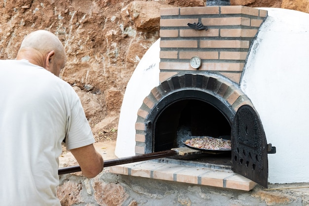 Man zet pizza in handgemaakte wit geschilderde houtoven buiten gebouwd met schop