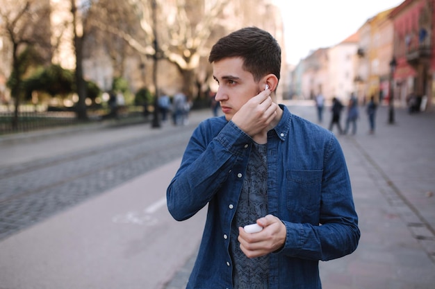 Man zette zijn draadloze koptelefoon op Knappe man in blauw shirt staat in het centrum van de stad