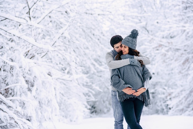 Man zijn mooie zwangere vrouw teder knuffelen in een besneeuwde winter park