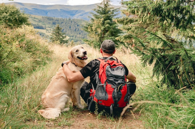 Foto man zit achteruit op trekking bergpad naast golden retriever hond