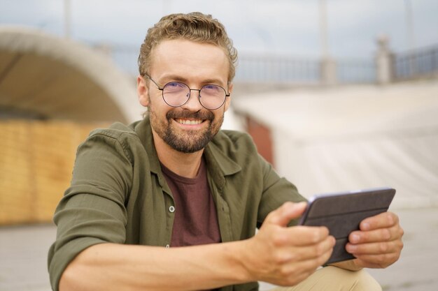 Man zit buiten op de trap met een charmante glimlach terwijl hij goed nieuws leest met een uitdrukking van pure vreugde