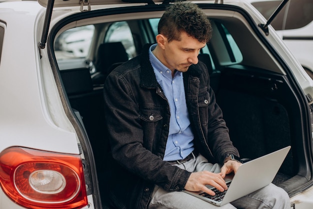 Man zit in de kofferbak van zijn auto en werkt op de computer