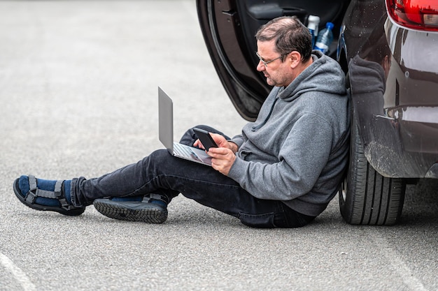 Man zit op asfalt met de auto en werkt op een laptop die op afstand werkt op reis